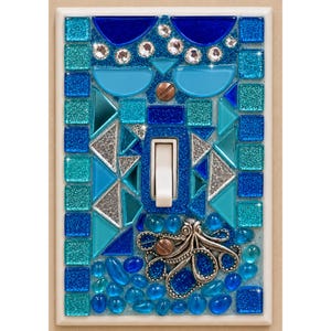 May include: A rectangular light switch cover decorated with a mosaic of blue, turquoise, and silver glass tiles. The design features clear rhinestones, a central white toggle switch, and a silver-toned metal octopus figurine at the bottom.