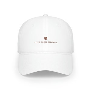 May include: White baseball cap with brown text that reads "LOVE THEM ANYWAY" and a brown smiley face above the text.