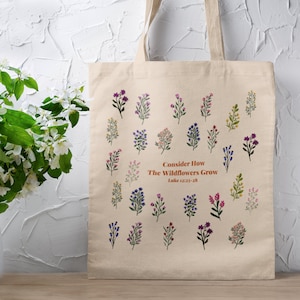 May include: A beige tote bag with a floral design and the text "Consider How The Wildflowers Grow Luke 12:27-28".