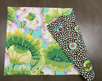 May include: A reversible placemat with a green and pink floral pattern on one side and a brown and green polka dot pattern on the other side.