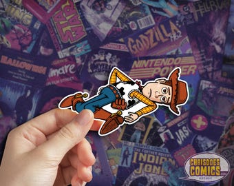 May include: A sticker featuring a cartoon illustration of Woody from Toy Story, lying down. He wears a brown cowboy hat, a yellow shirt, a cow-print vest, blue jeans, and brown boots. The sticker is held against a background of vintage comic book covers.