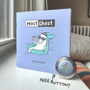 May include: A blue book with the title "Most Ghost" and an illustration of a ghost wearing sunglasses and a hat, floating on a blue and white polka dot inner tube. The book is on a white surface with a silver pin that says "Official Most Ghost Spiritual Supporter" on it.