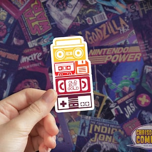 May include: A sticker featuring a stack of retro electronics, including a boombox, cassette player, floppy disk drive, and a video game console. The sticker is layered with a gradient of red, orange, yellow, and white.