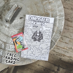 May include: A black and white comic book titled "Dinosaur Jones: A Prehistorically Bad Influence" by Chris MP. A red and black trading card with a dinosaur character is included.