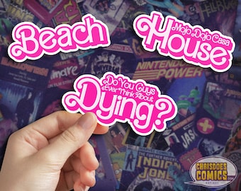 May include: Three pink and white stickers with text: "Beach", "Mojo Dojo Casa House", and "Do You Guys Ever Think About Dying?". The stickers are held against a background of colorful comic book covers.