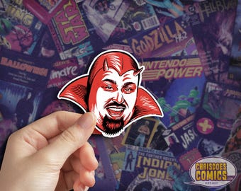 May include: A red and white sticker featuring a smiling devil-like character with horns and a goatee. The sticker is held in front of a background of comic book covers. The sticker is from ChrisDoesComics.