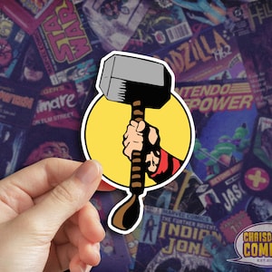 May include: A yellow circle sticker with a black and gray cartoon hammer and a red and black cartoon hand holding the hammer.