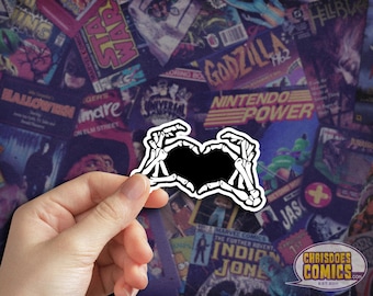 May include: Black and white sticker of two skeletal hands forming a heart shape. The sticker is on a background of colorful comic book covers.