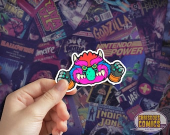 May include: A colorful sticker featuring a cartoon monster with pink fur, red hair, green eyes, and a toothy grin. The monster is wearing a blue and black arm band and is holding a blue and black fist. The sticker is placed on a background of vintage comic book covers.
