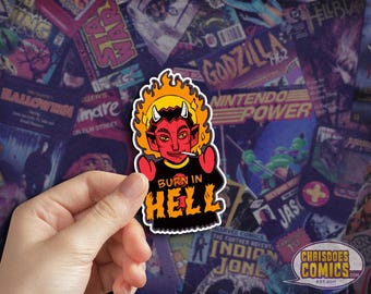 May include: A sticker featuring a cartoon devil with red skin, horns, and a cigarette. The devil is wearing a black shirt with the words "BURN IN HELL" in orange and yellow. The background is a collage of comic book covers.