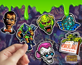 May include: A set of eight horror-themed enamel pins featuring characters like Chucky, Jason Voorhees, and a creature from the black lagoon. The pins are colorful and have a glossy finish. The text on the sign reads "Welcome to Horrorland Where Nightmares Come to Life!"