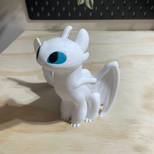Op de afbeelding: Witte plastic figuur van een draak met blauwe ogen. De draak heeft vleugels en staat op alle vier poten.