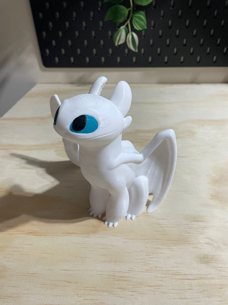 Op de afbeelding: Witte plastic figuur van een draak met blauwe ogen. De draak heeft vleugels en staat op alle vier poten.