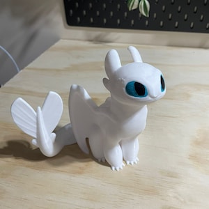 Op de afbeelding: Witte plastic figuur van een draak met blauwe ogen. De draak heeft een lange staart en vleugels.
