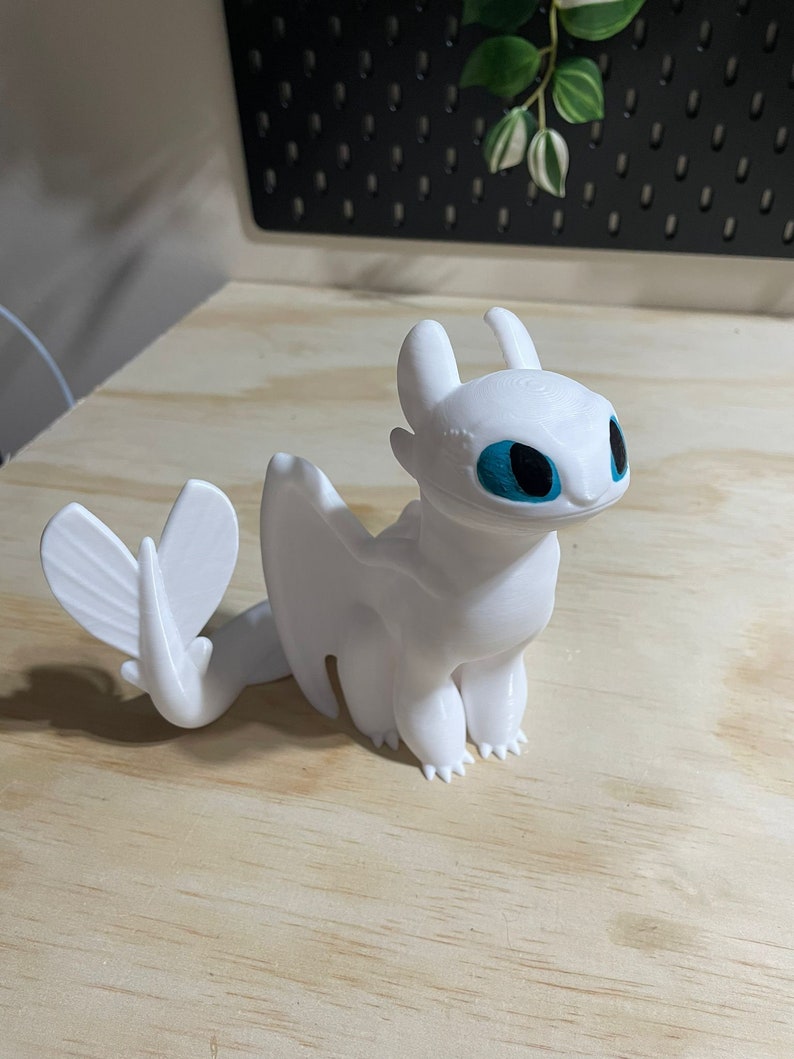 Op de afbeelding: Witte plastic figuur van een draak met blauwe ogen. De draak heeft een lange staart en vleugels.