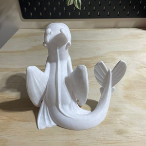 Op de afbeelding: Witte 3D-geprinte figuur van een draak met vleugels en een staart die om zijn lichaam is gekruld. De draak zit op een houten oppervlak.