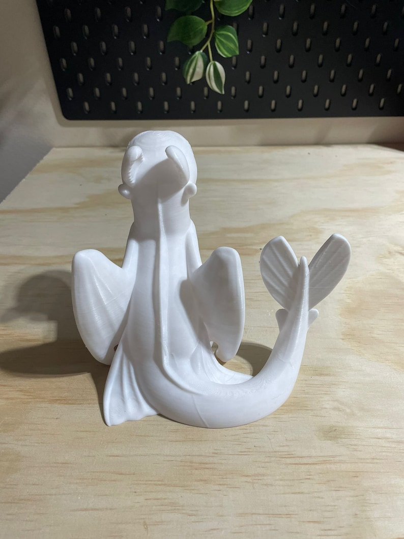 Op de afbeelding: Witte 3D-geprinte figuur van een draak met vleugels en een staart die om zijn lichaam is gekruld. De draak zit op een houten oppervlak.