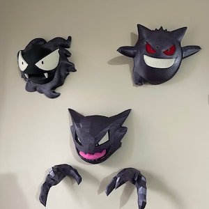 以下が含まれることがあります： 3Dプリントされたポケモンのフィギュア3体。黒と白のゲンガー、紫と白のゲンガー、紫とピンクのゴース。フィギュアは壁に取り付けられています。