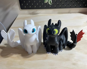 May include: Two dragon figurines, one white with blue eyes and one black with green eyes. The white dragon has a red tail fin.