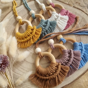 Op de afbeelding: Zes houten ringen met kleurrijke macramé franjes. De ringen zijn aan elkaar geregen met koorden en hebben houten kralen.