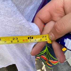 May include: A close-up of a white and purple shirt with a yellow measuring tape. The tape measures 25 inches.
