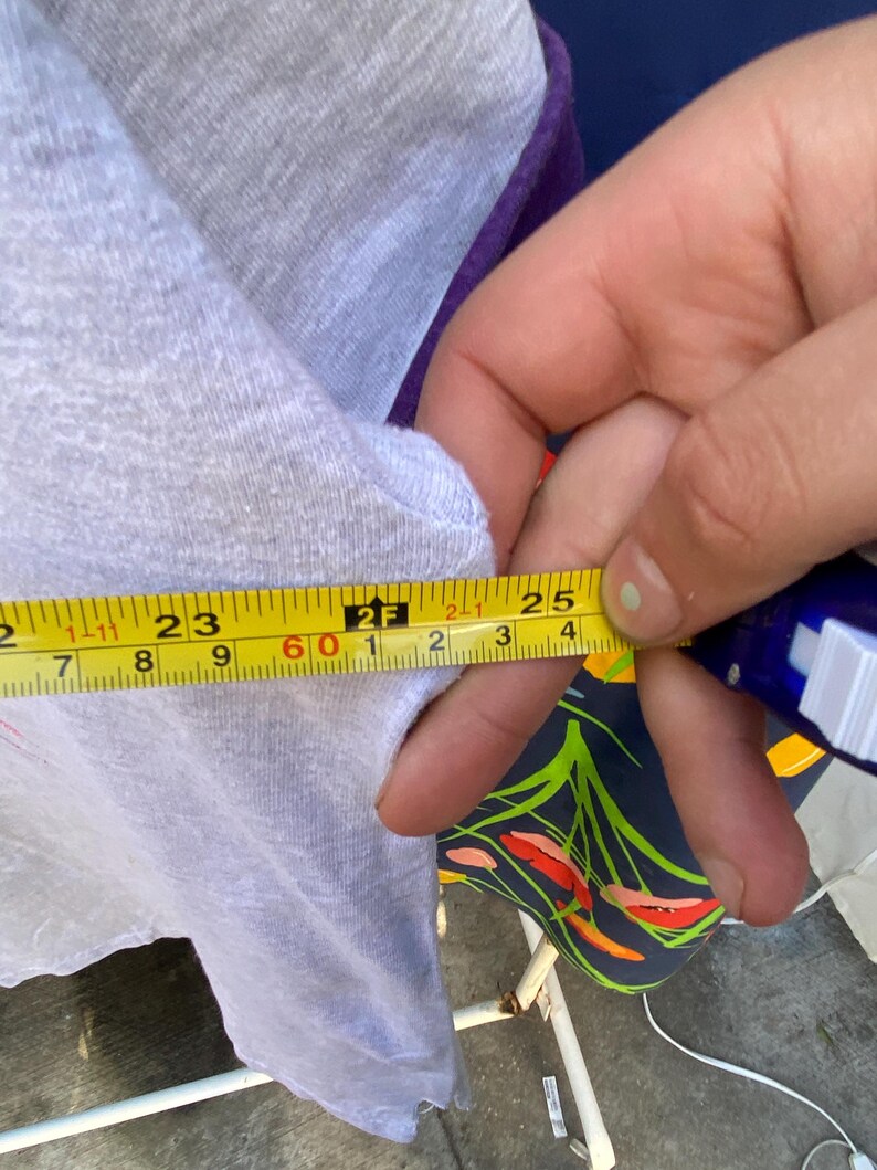 May include: A close-up of a white and purple shirt with a yellow measuring tape. The tape measures 25 inches.