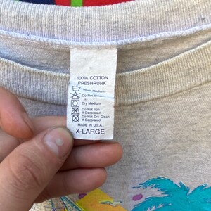 May include: A gray t-shirt with a palm tree and sunset graphic. The tag says "100% Cotton Preshrunk" and "X-Large".