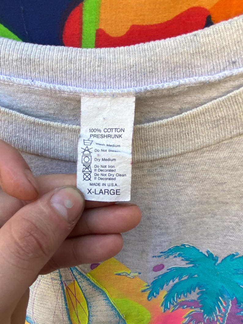 May include: A gray t-shirt with a palm tree and sunset graphic. The tag says "100% Cotton Preshrunk" and "X-Large".