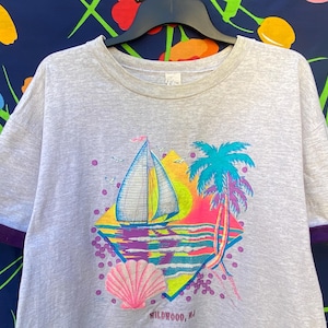 May include: Gray t-shirt with a colorful graphic of a sailboat, palm tree, and seashell. The graphic is in a diamond shape with the text "Wildwood, NJ" at the bottom.