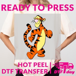 May include: A DTF transfer featuring a cartoon tiger character in orange, black, and yellow. The text "READY TO PRESS" is at the top, and "HOT PEEL DTF TRANSFER" is at the bottom. The image also includes a graphic of a truck.