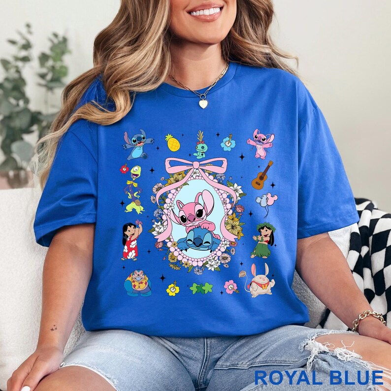May include: Royal blue t-shirt with a vibrant cartoon graphic. The design showcases a central oval frame with two characters, surrounded by floral details and other characters. The text "ROYAL BLUE" is displayed at the bottom of the shirt.