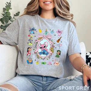 May include: Sport grey t-shirt with a vibrant cartoon graphic. The design features a pink and blue alien couple in a floral frame, surrounded by other characters and musical instruments. The text "SPORT GREY" is at the bottom of the shirt.