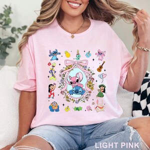May include: Pale pink t-shirt with a cartoon graphic of Stitch and Angel, framed by flowers and other characters. The words "LIGHT PINK" are printed at the bottom. A fun, colourful design.