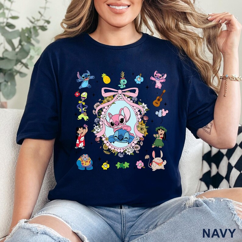 May include: Navy blue t-shirt with a colourful graphic of cartoon characters. The design includes a central oval frame with two characters, surrounded by floral elements and other characters. The word "NAVY" is printed at the bottom of the shirt.