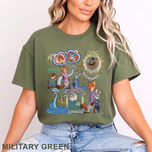 May include: Military green t-shirt with a vibrant graphic of Zootopia characters. The design showcases detailed illustrations of animal characters, with the word "Zootopia" in green. The t-shirt is a crew neck style, perfect for casual wear.