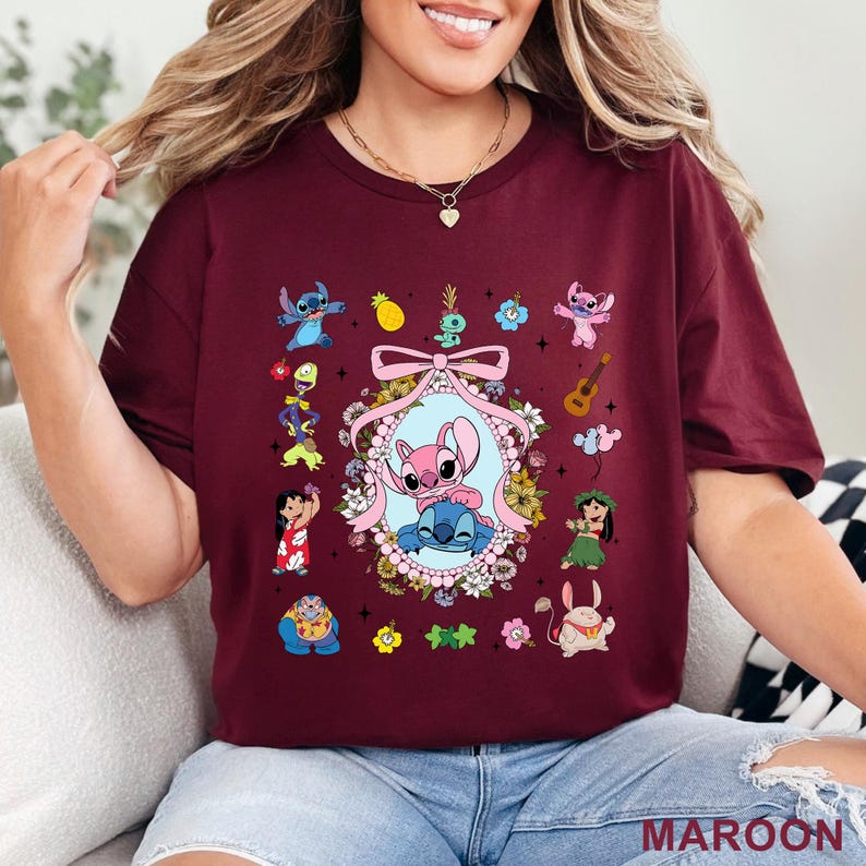 May include: Maroon t-shirt with a colourful graphic of Stitch and Angel characters surrounded by flowers and other elements. The design includes a pink bow and the word "MAROON" at the bottom.