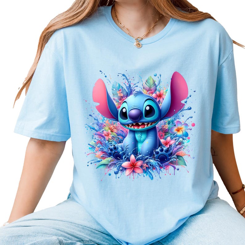 May include: Light blue t-shirt featuring a vibrant graphic of the character Stitch surrounded by colorful flowers and water splashes. The design includes shades of blue, pink, and purple, creating a playful and eye-catching aesthetic. The shirt has short sleeves and a crew neck.