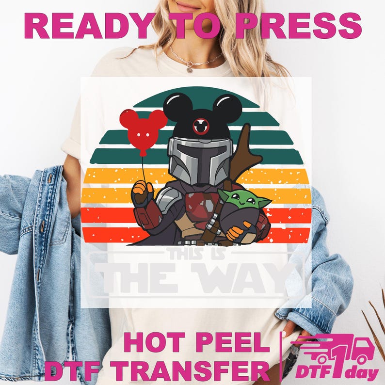 May include: White t-shirt featuring a graphic of The Mandalorian with a Mickey Mouse-themed helmet and Grogu. The design includes a red balloon, a sunset background, and the text "THIS IS THE WAY". The words "READY TO PRESS" and "HOT PEEL DTF TRANSFER" are also visible.