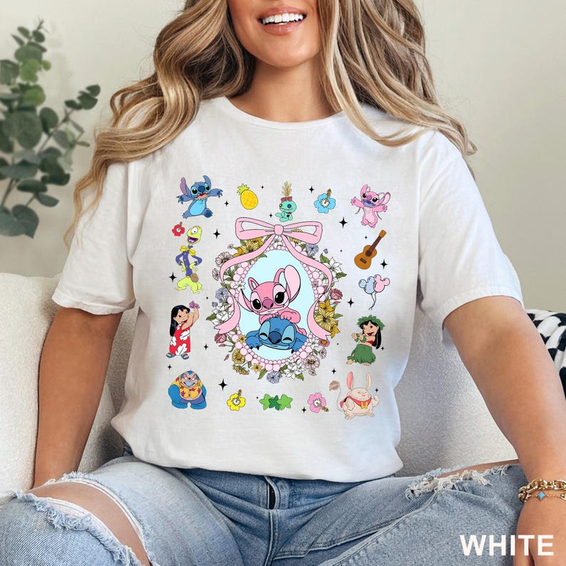 May include: White t-shirt with a vibrant graphic of cartoon characters, including Stitch and Angel, set within a floral frame. The word "WHITE" is printed in the bottom right corner.