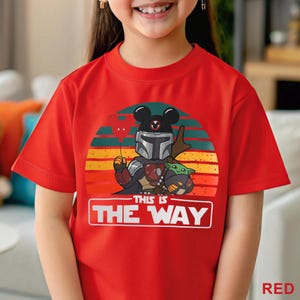 May include: Red t-shirt featuring a graphic of a Mandalorian character with Mickey Mouse ears, holding a heart-shaped balloon, and Grogu. The design is set against a sunset backdrop with the text "THIS IS THE WAY".