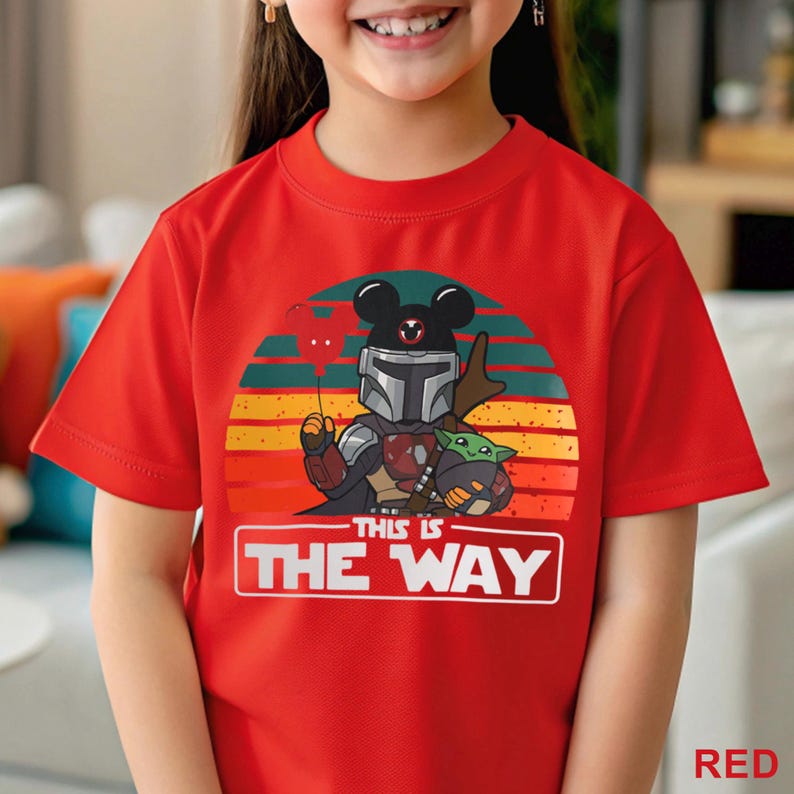 May include: Red t-shirt featuring a graphic of a Mandalorian character with Mickey Mouse ears, holding a heart-shaped balloon, and Grogu. The design is set against a sunset backdrop with the text "THIS IS THE WAY".