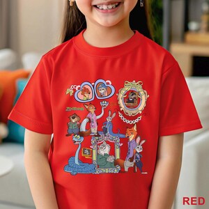 May include: A red t-shirt with a vibrant graphic of characters from the film "Zootropolis." The design showcases animal characters in frames and scenes, with the word "Zootopia" in green. The shirt is made of a soft material.