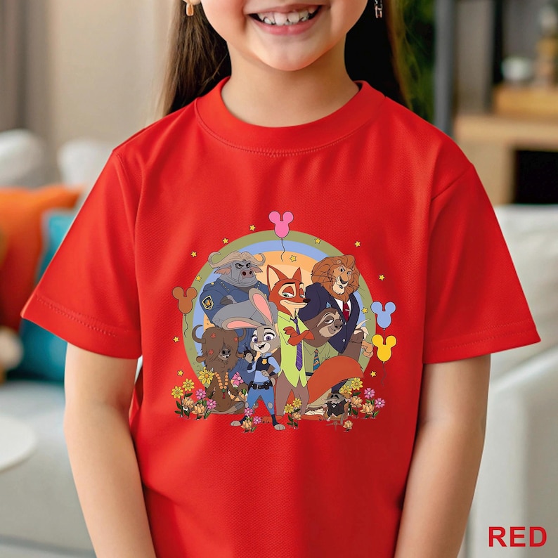 Puede incluir: Una camiseta roja con un estampado de personajes de la pel&iacute;cula "Zootr&oacute;polis". El dise&ntilde;o incluye a Judy Hopps, Nick Wilde y otros personajes animales, rodeados de flores y un arco&iacute;ris. La palabra "RED" est&aacute; impresa en la parte inferior.
