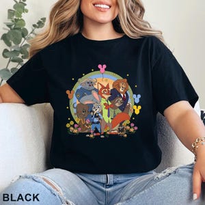 Puede incluir: Camiseta negra con un gr&aacute;fico colorido de personajes de la pel&iacute;cula animada Zootopia. El dise&ntilde;o incluye a Judy Hopps, Nick Wilde y otros personajes, rodeados de flores y un arco&iacute;ris. La palabra "BLACK" est&aacute; impresa en la parte inferior.