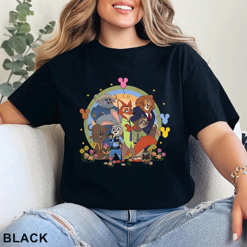Puede incluir: Camiseta negra con un gr&aacute;fico colorido de personajes de la pel&iacute;cula animada Zootopia. El dise&ntilde;o incluye a Judy Hopps, Nick Wilde y otros personajes, rodeados de flores y un arco&iacute;ris. La palabra "BLACK" est&aacute; impresa en la parte inferior.