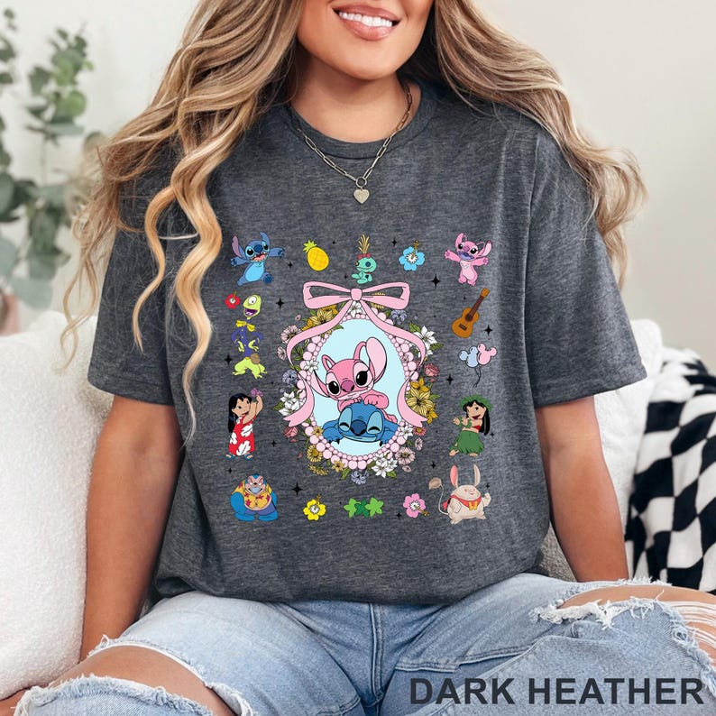 May include: Dark grey t-shirt with a colourful cartoon character graphic. The design features a central oval with two characters, surrounded by flowers and other characters. The text "DARK HEATHER" is at the bottom.