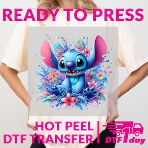 May include: A light-colored t-shirt featuring a vibrant graphic of a blue cartoon character with large ears, surrounded by colorful flowers and water splashes. The text "READY TO PRESS" and "HOT PEEL DTF TRANSFER" are displayed in pink and white.