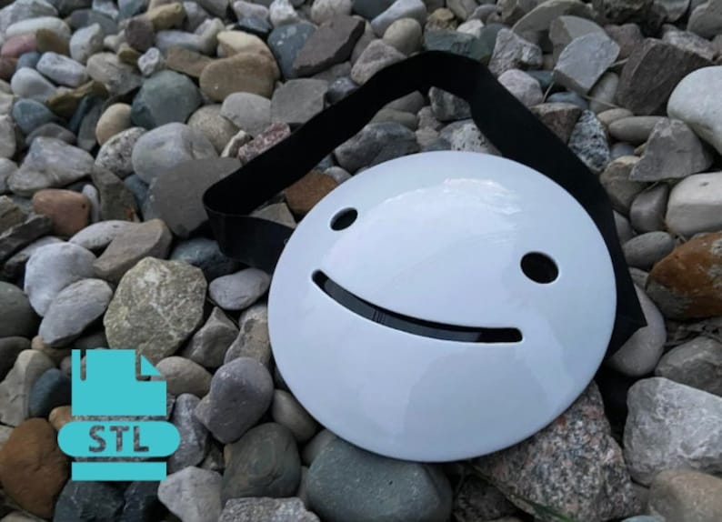 May include: White plastic mask with a black smiling face. The mask is on a bed of small gray rocks.