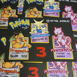 May include: Three Pokemon trading cards featuring Dragonite, Alakazam, and Mewtwo. The cards are black with a yellow border and feature illustrations of the Pokemon with their names and abilities. The cards are numbered 3.