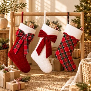 May include: Three Christmas stockings hanging from a wooden frame. The first is red velvet with a plaid bow, the second is white quilted fabric with a red velvet bow, and the third is red and green plaid fabric. Each has a white cuff.